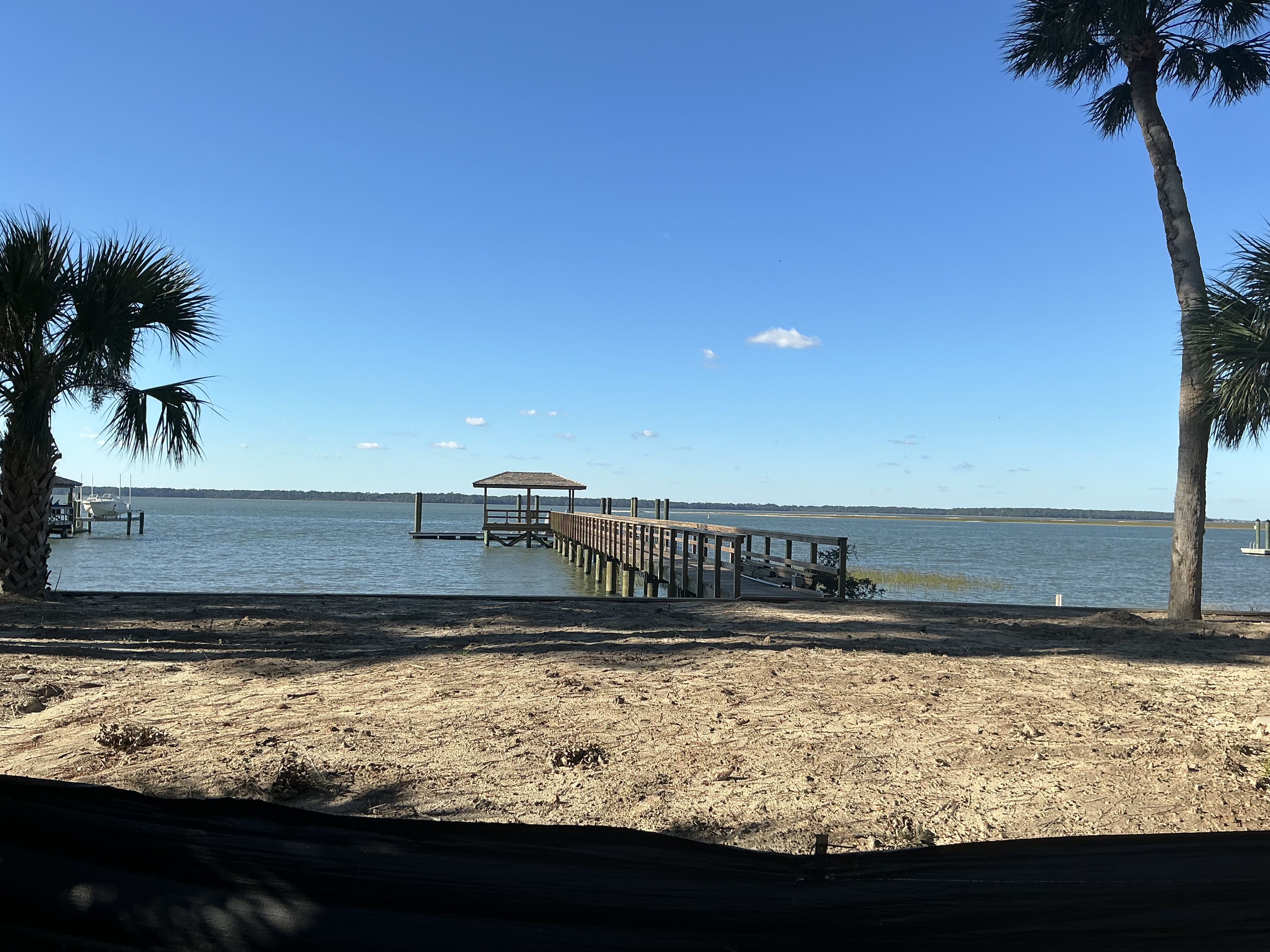 Wooden pier with a covered gazebo reaching into calm coastal water, palms framing the shoreline