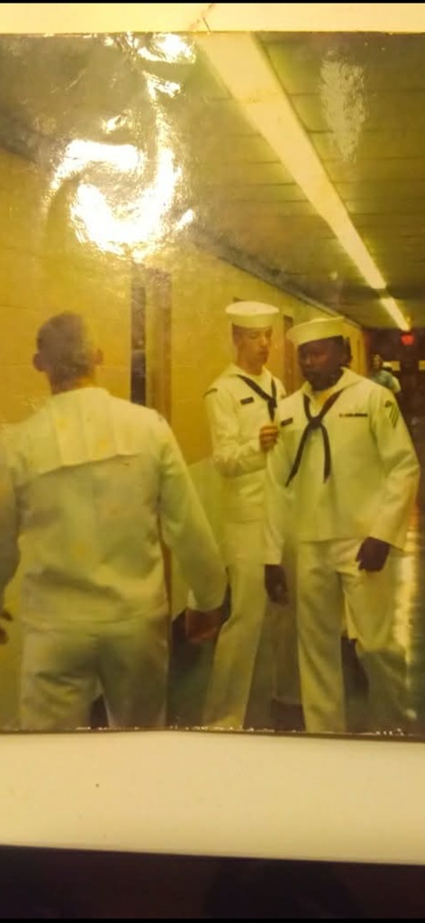 Three United States Navy sailors in white dress uniforms standing in a passageway aboard ship