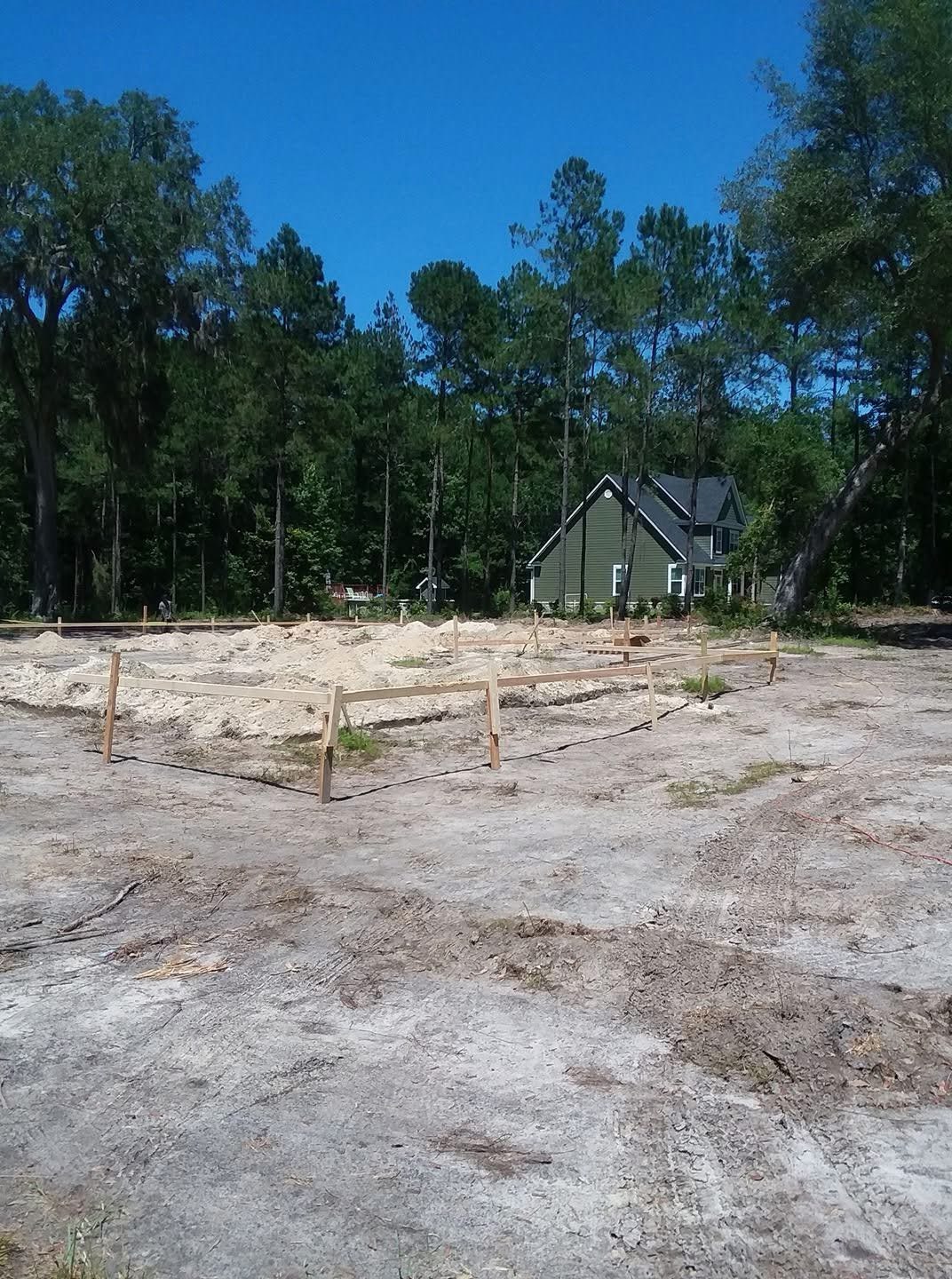 First solo ground-up build — laying out the lot, the stake-and-board outline set over the sand pad with the green house beyond