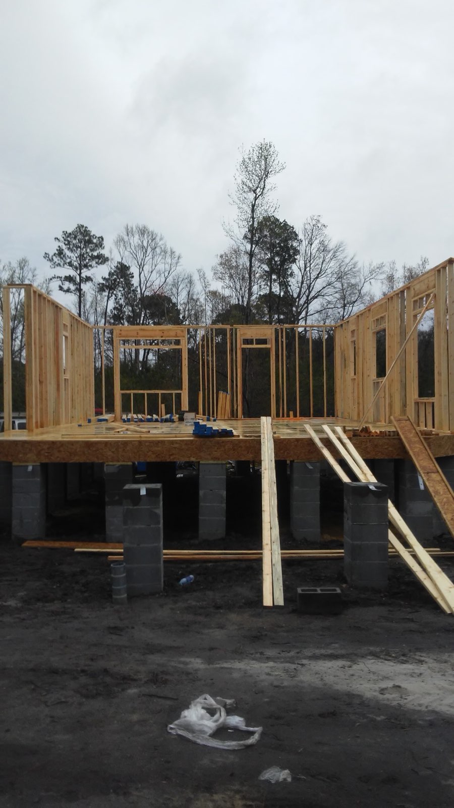 Early framing stage — plywood subfloor on cinder-block piers with unfinished walls and window frames