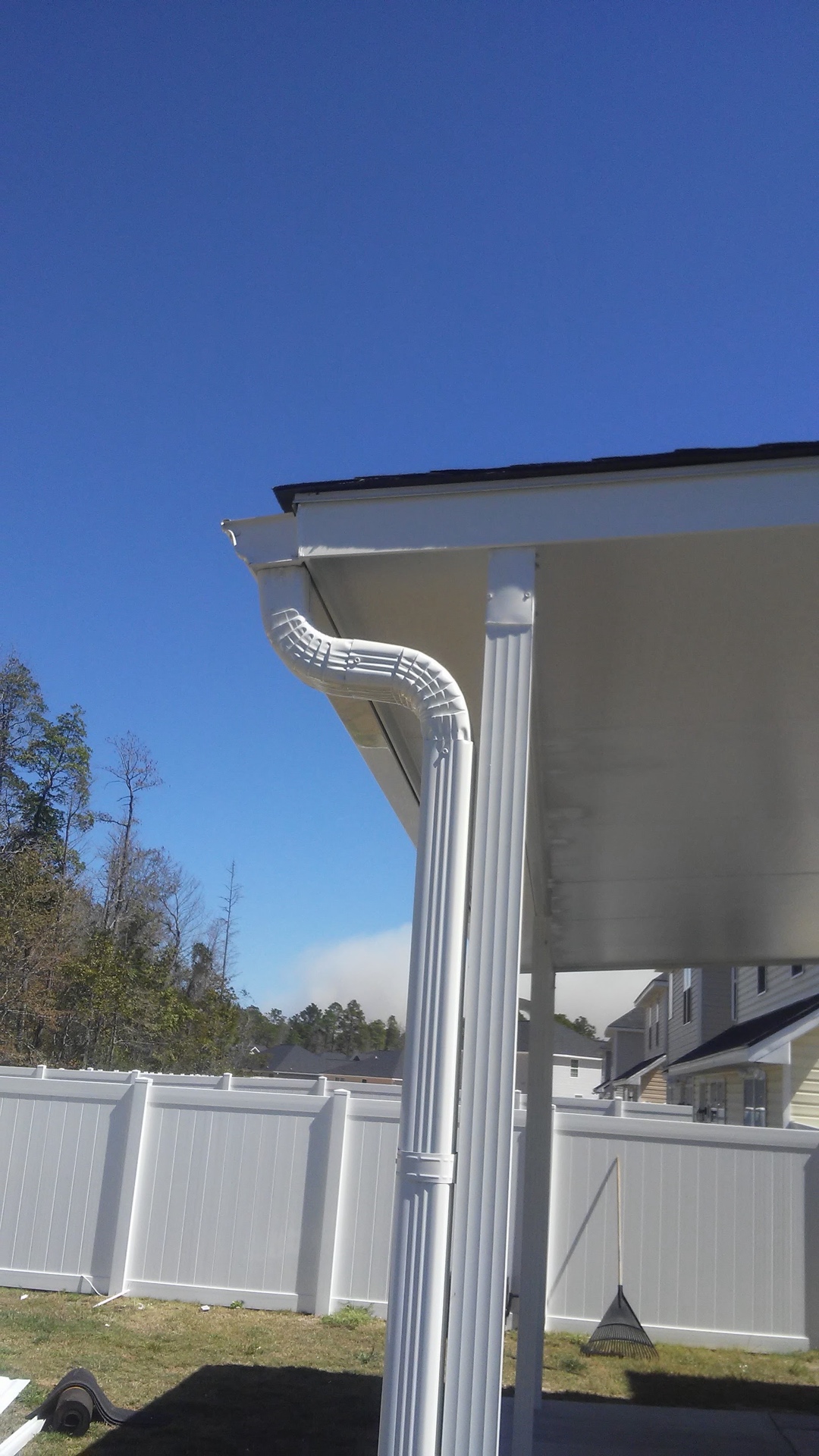 The new white gutter and downspout joined on the corner of the cover under a clear blue sky