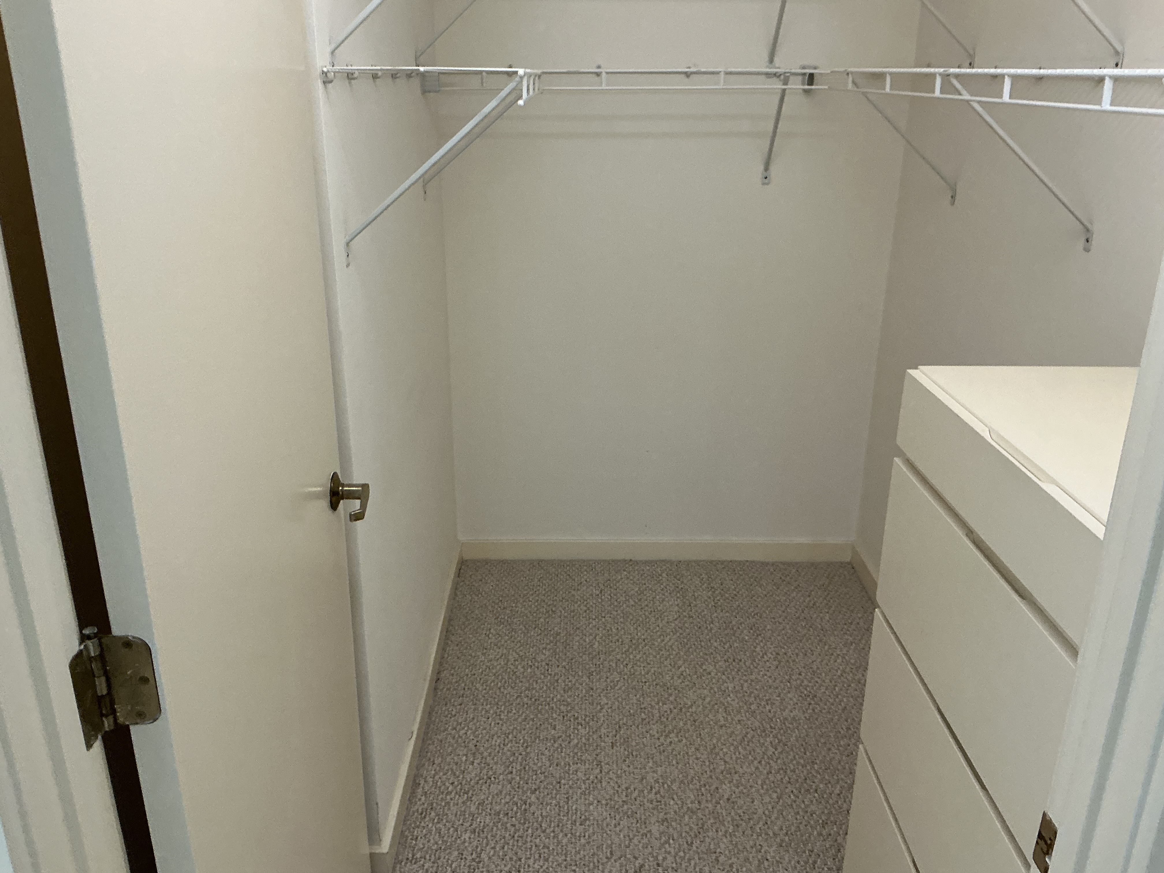 Original closet with white wire shelving and hanging rods, with the built-in drawer unit on the right — the door open showing its hinge and doorknob — before the remodel