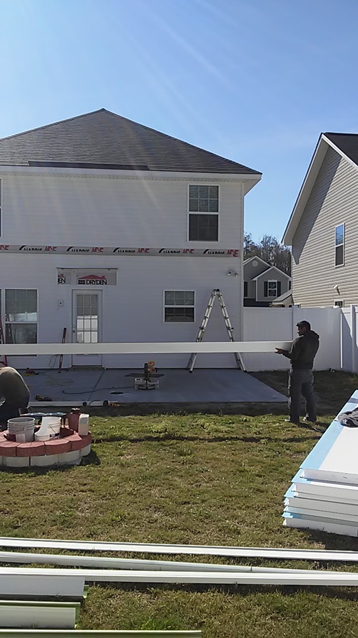 Two crew members carrying a long white panel across the new slab, a ladder against the house behind them