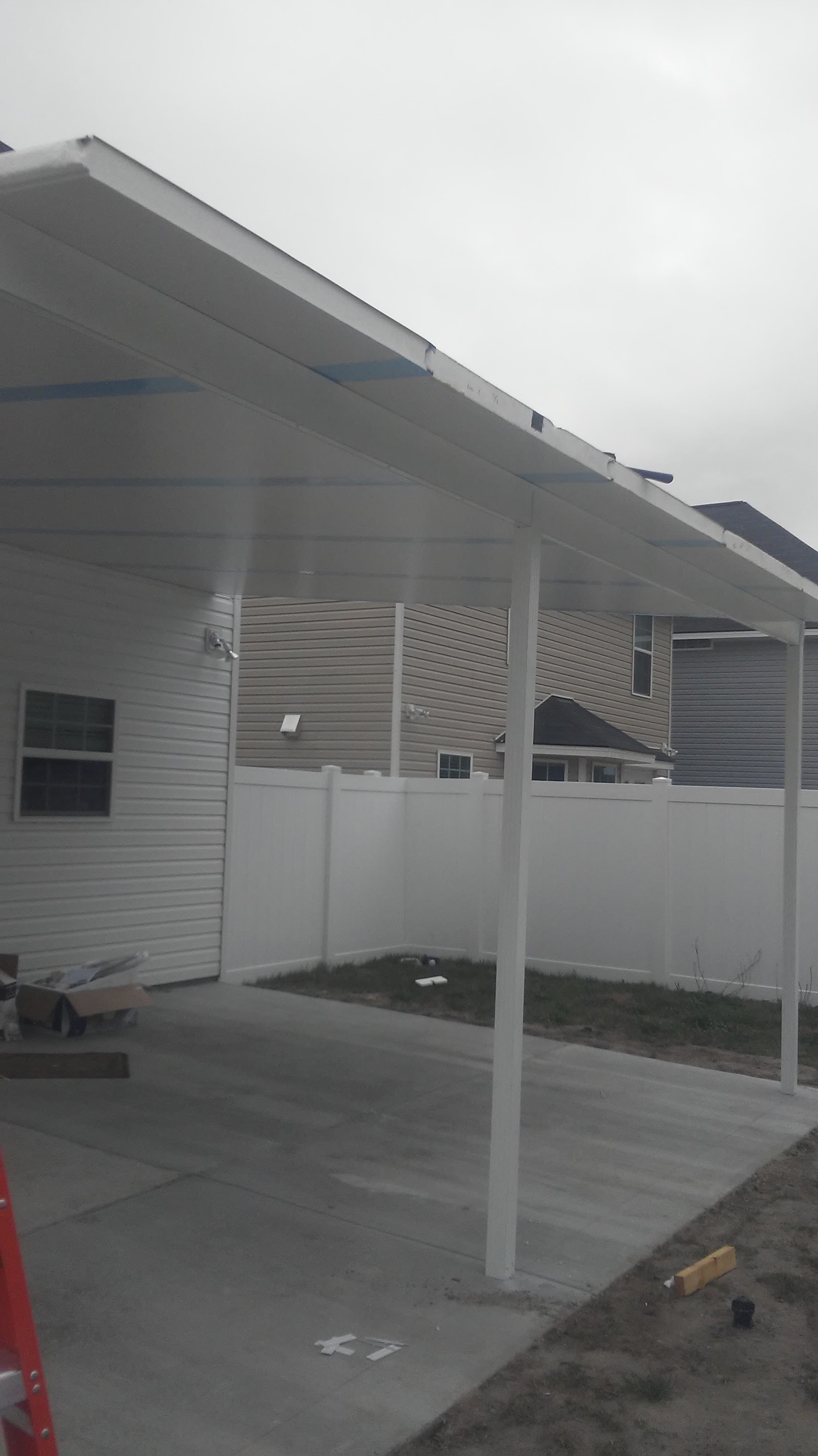 The white metal cover standing on its posts over the new pad, seen from underneath, the white privacy fence behind it