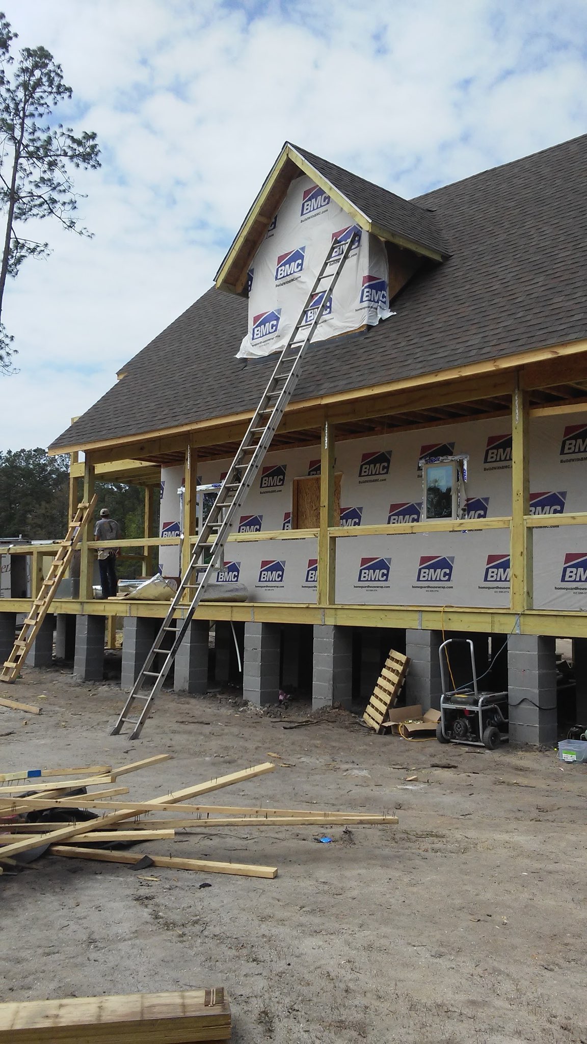 New construction — wrapped and drying in: a raised Low Country home framed, roofed and sheathed, with ladders still up on the gable