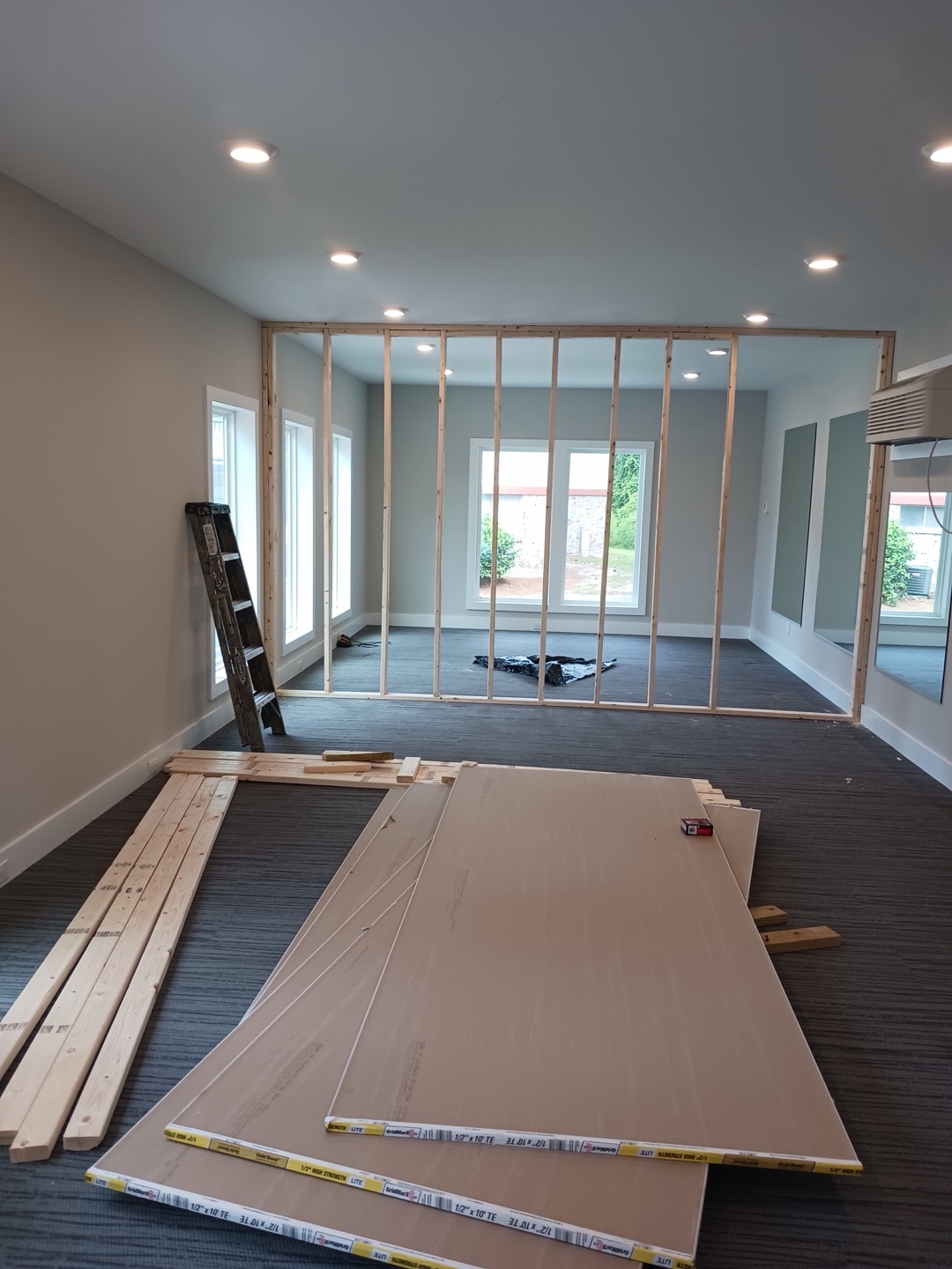 Tenant improvements in the same building — a new partition wall framed on its studs inside the office suite, with sheets of drywall stacked on the carpet and a ladder against the wall