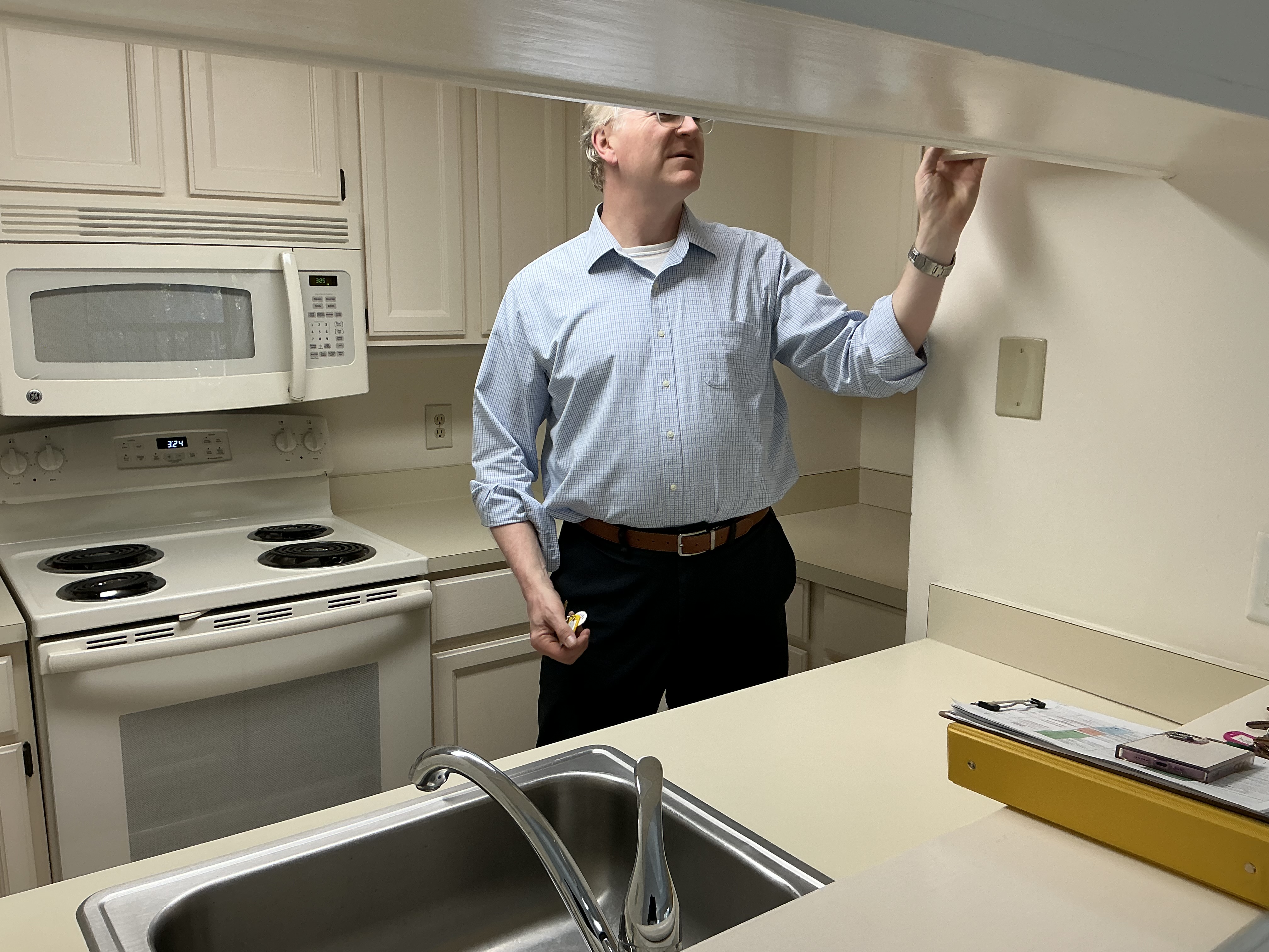 The homeowner at the initial walkthrough, inspecting the upper cabinets in the original kitchen