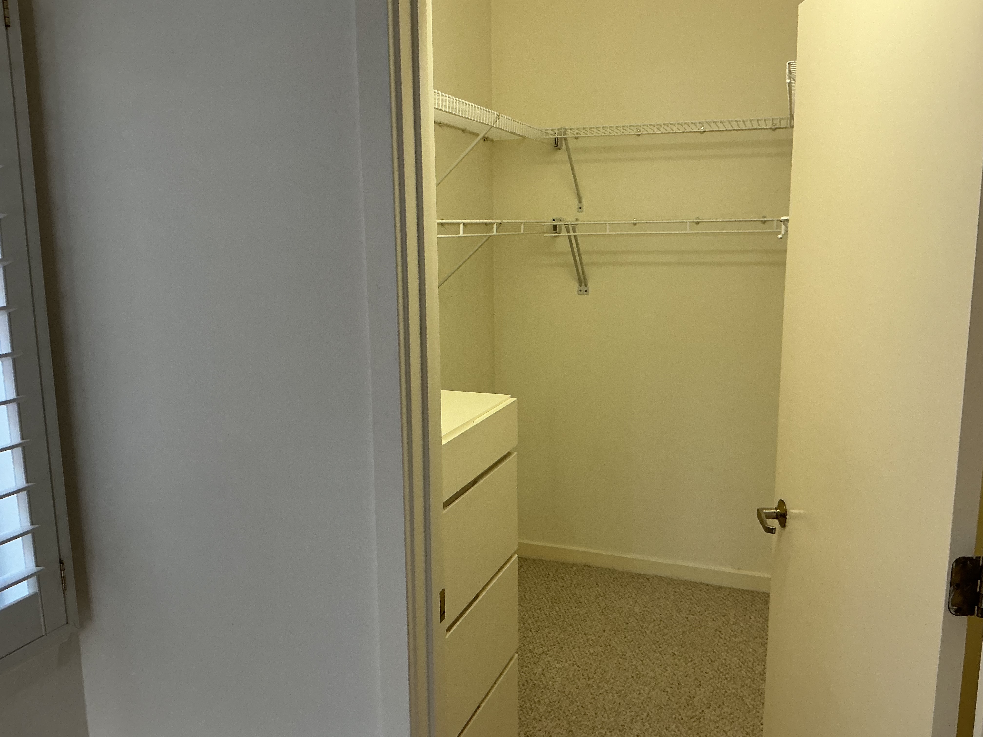 Original closet with wire shelving and a dresser on pale yellow walls