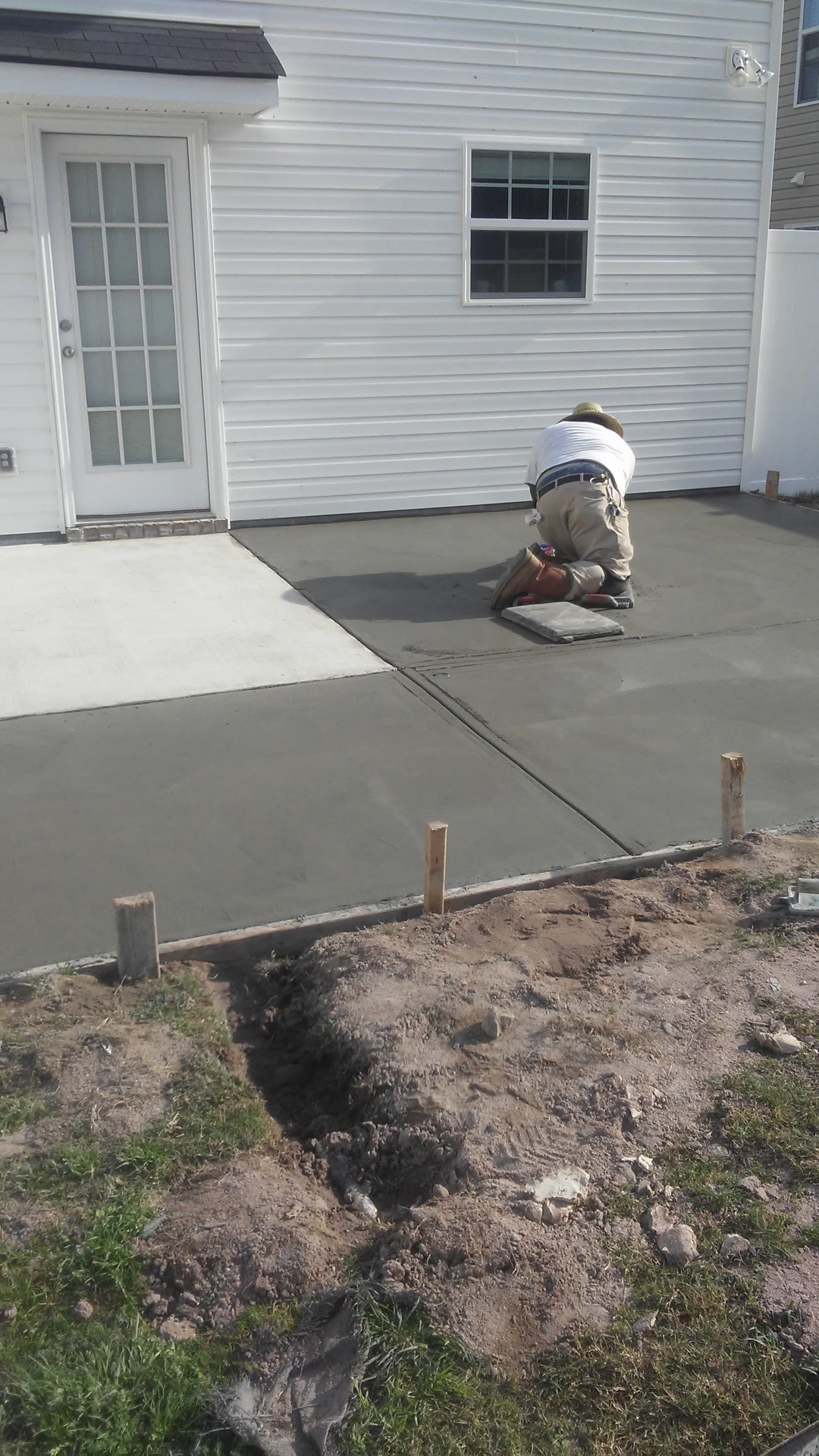A crew member kneeling on the freshly poured concrete, working the surface, with wooden stakes holding the edge of the new slab