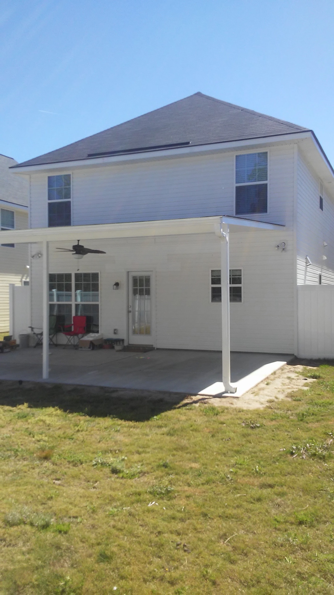 The finished addition — the concrete patio under its white cover, the ceiling fan overhead and the new downspout on the corner, seen from the yard
