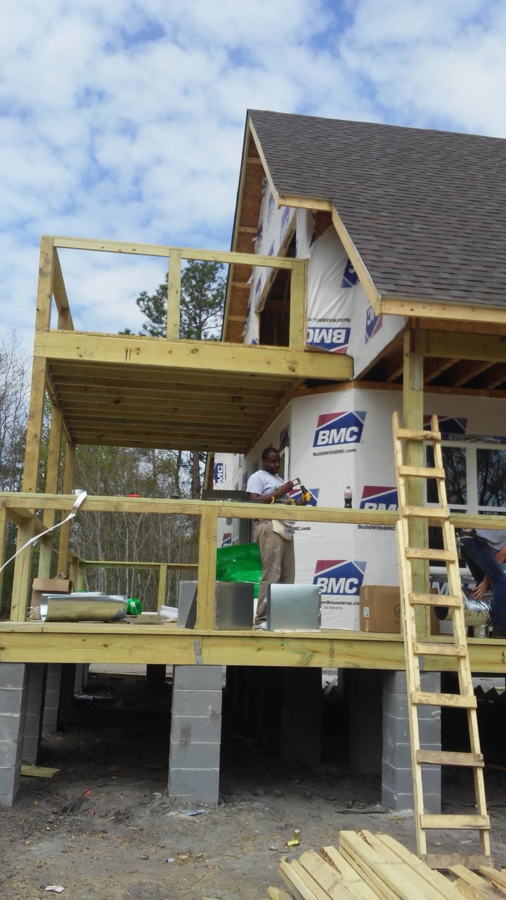 General contracting on site — a crew member installing ductwork on the raised deck of a home under construction